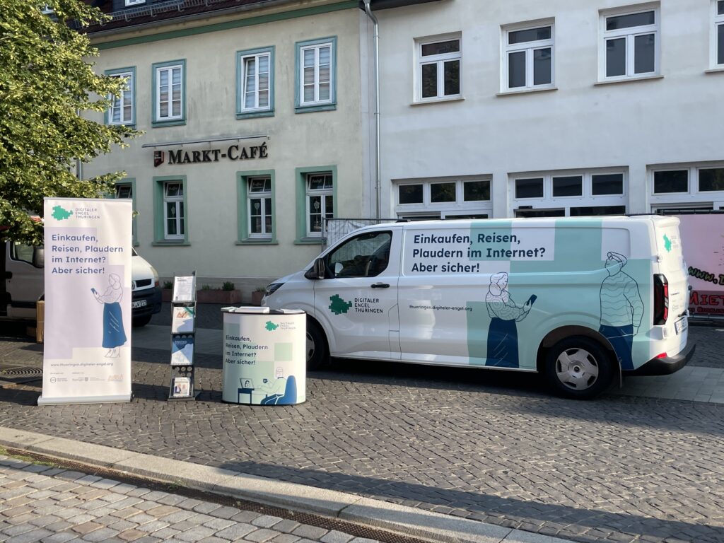 Das Auto vom Digitalen Engel Thüringen mit Aufschrift über sicheres Einkaufen und Reisen im Internet, umgeben von Werbematerialien auf dem Marktplatz von Sömmerda.