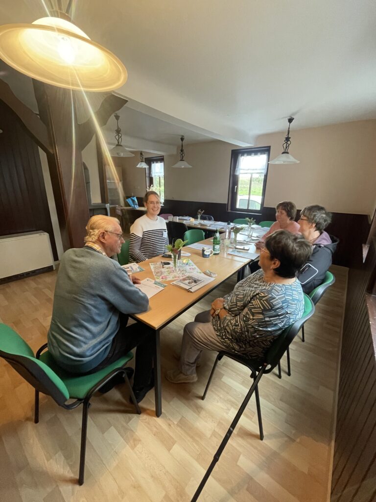 Eine kleine Grupper älterer Menschen sitzen zusammen mit Martina an einem Tisch im Bürgerhaus Kleinwelsbach.