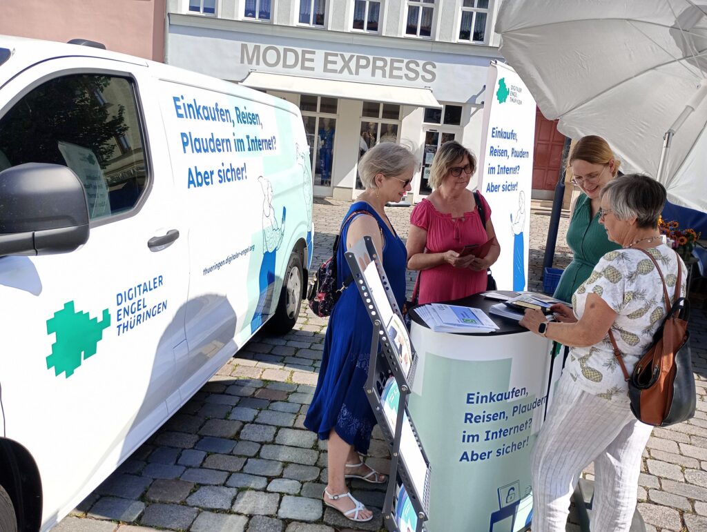 Auto des Digitalen Engel Thüringen mit Informationsstand. Die Referentin erklärt drei Besucherinnen etwas.