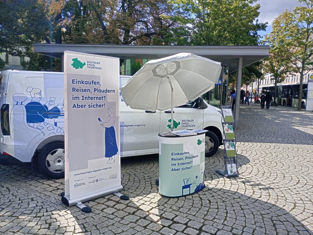 Auto des Digitalen Engel Thüringen mit Informationsstand auf einem Platz. Die Sonne scheint.