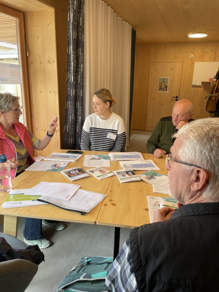 Martina sitzt mit drei älteren Menschen an einem runden Tisch.