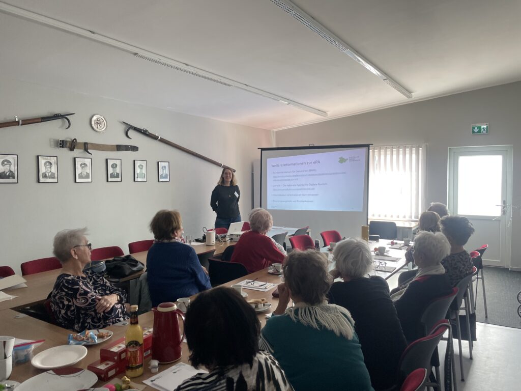 Martina steht in einem Raum vor einer Gruppe Senior:innen.