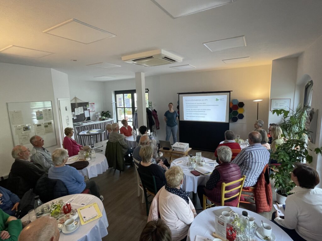 Martina steht vor einer Gruppe Senior:innen in der Begegnungsstätte und hält einen Vortrag,