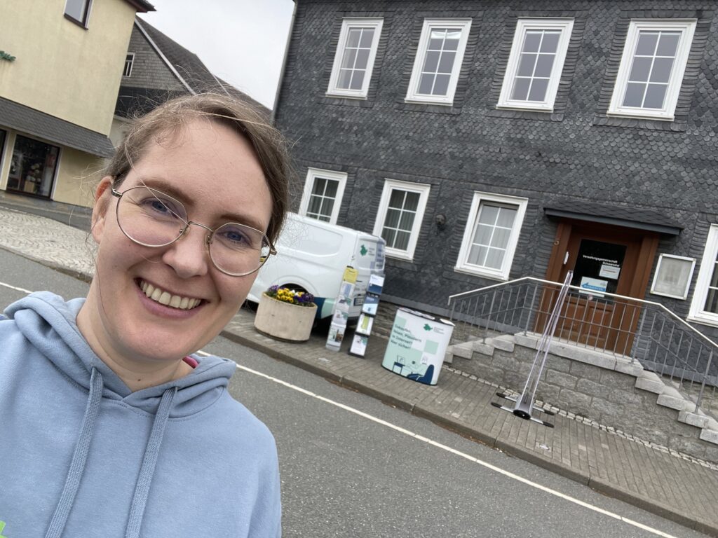 Ein Selfie von Martina vor dem Stand des Digitalen Engels Thüringen, der im Hintergrund aufgebaut ist.