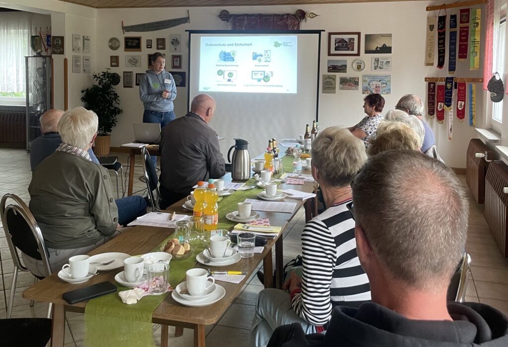 MArtina steht vor einer Gruppe älterer Menschen, die an einem mit Kaffee eingedeckten Tisch sitzen.