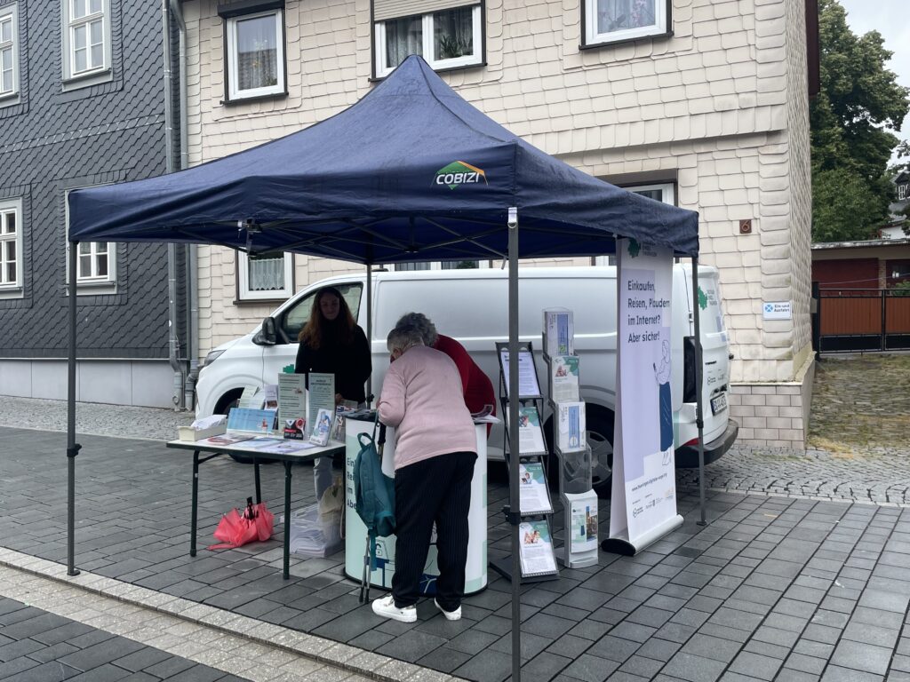 Der Stand des Digitalen Engel Thüringen auf einer Straße. Über den Stand ist ein PAvillion aufgebaut. Zwei Personen stehen am Stand.