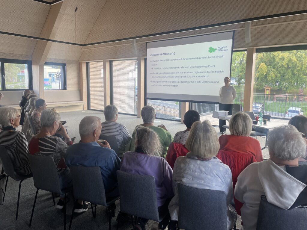 Eine Versammlung von Personen sitzt vor einem Bildschirm in bequemen Stühlen.