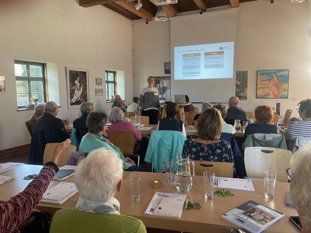 Mehrere Personen sitzen in einem Raum mit Holzbalkendecke und schauen auf eine Präsentation an der Wand.