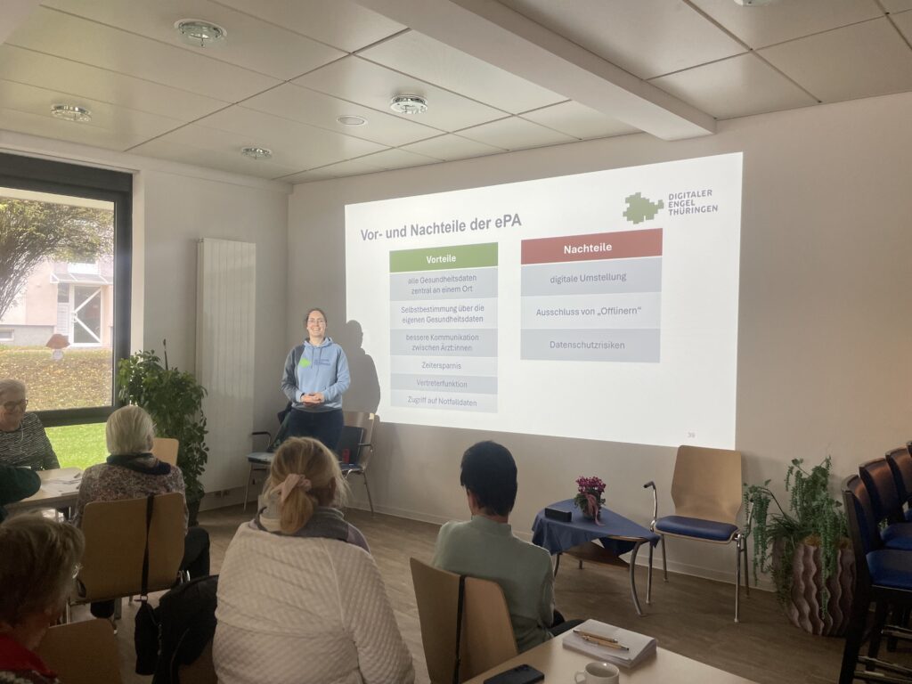 Gruppe älterer Menschen steht vor einem weißen Lieferwagen mit Text auf der Seite auf einem gepflasterten Platz in einer Kleinstadt.