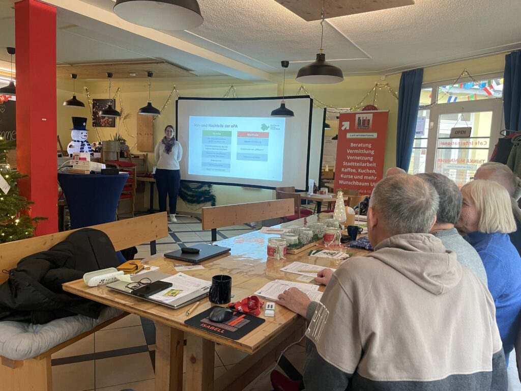 Frau steht vor Leinwand mit Präsentation, mehrere Personen sitzen an Holztisch mit Unterlagen und Getränken in hellem Raum mit Weihnachtsdeko.