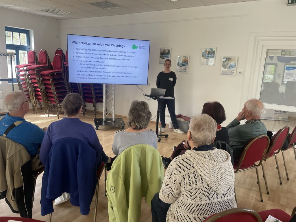 Martina steht vor einer Gruppe älterer Menschen, die in einem Kreis zusammensitzen.