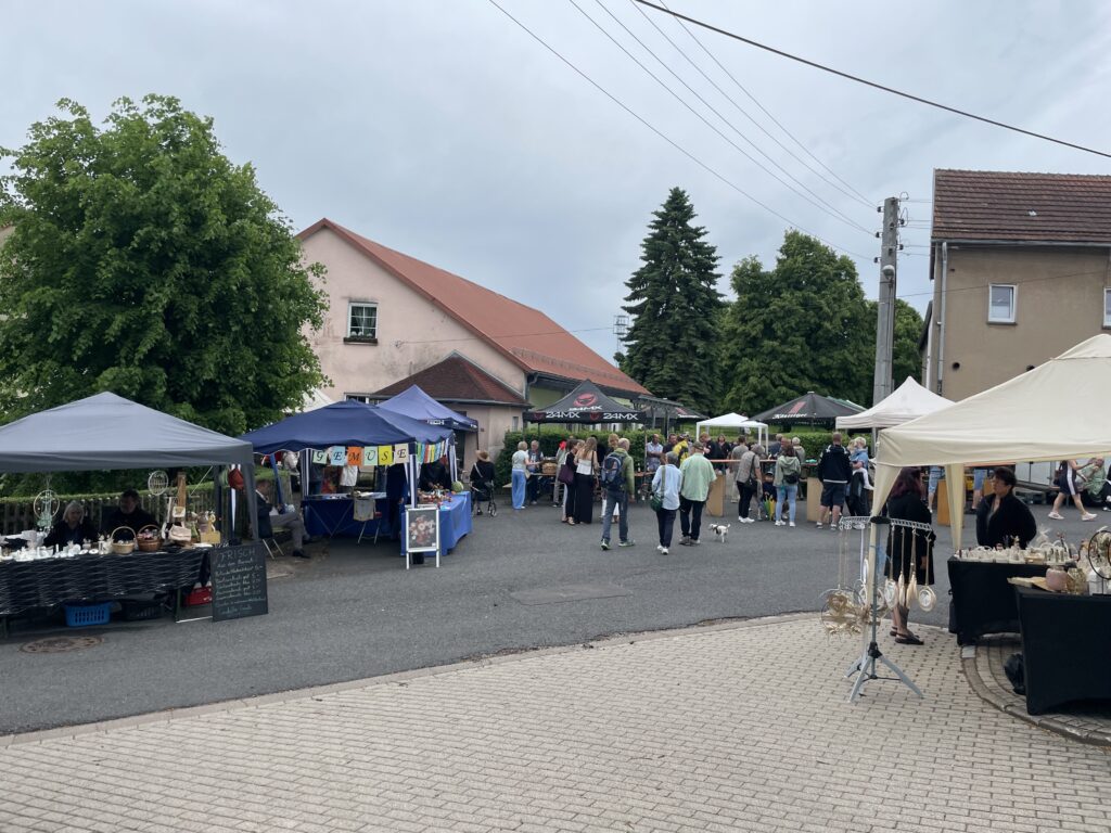 Marktstände mit Menschen auf einem gepflasterten Platz vor Wohnhäusern an einem bewölkten Tag